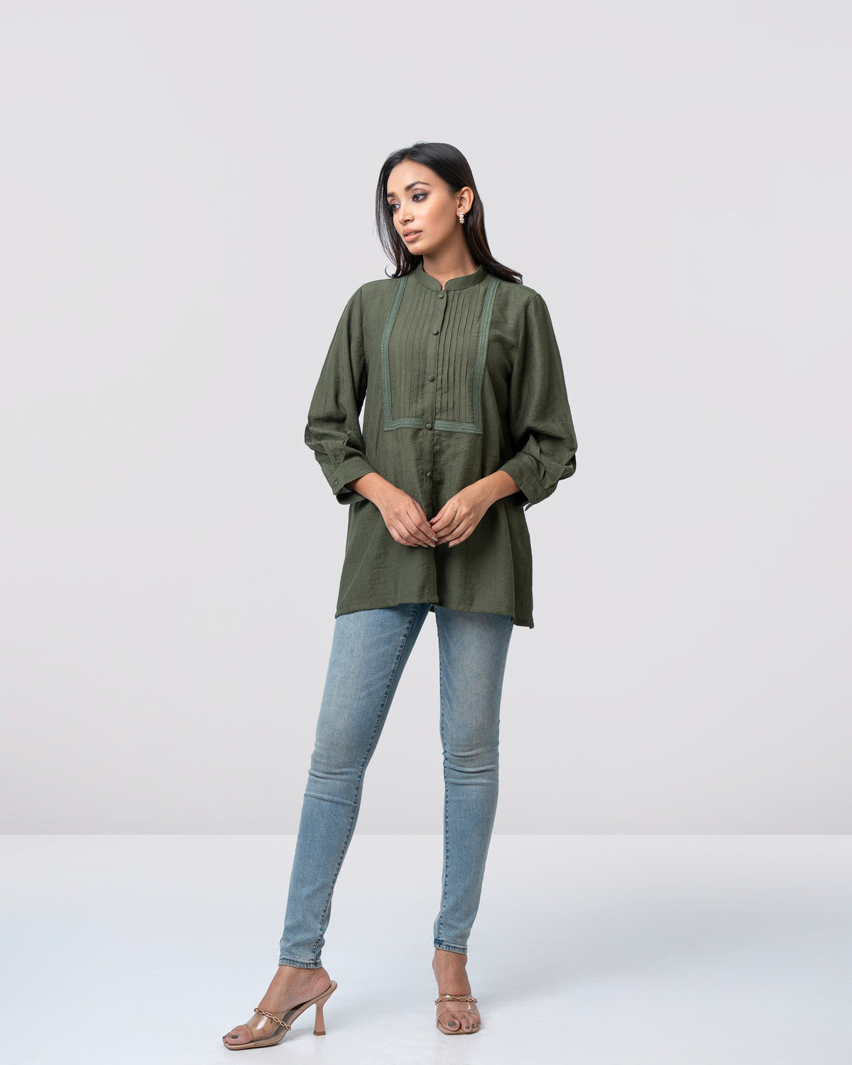 Woman wearing a green long-sleeve top and blue jeans on a white background